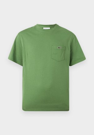Grünes T-Shirt mit kurzen Ärmeln und Rundhalsausschnitt, das eine Tasche auf der linken Brustseite mit einem kleinen, gestickten Krokodil-Logo aufweist.