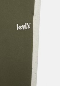 Olive Zielona tkanina bawełniana z białą panelą z polaru; z przodu haftowane logo "Levi's" w białym kolorze. Gładka tekstura, casualowy design.