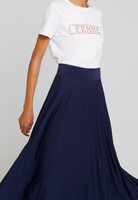 Maglietta bianca con stampa rossa "FEMME", abbinata a una lunga gonna fluida a pieghe di un blu navy scuro con cintura elastica.