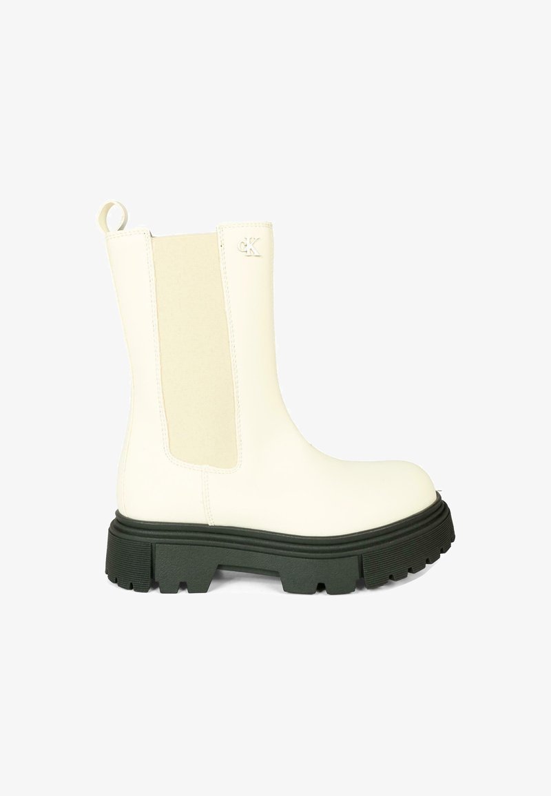 Bottine blanche avec semelle en caoutchouc verte, panneaux latéraux élastiques et tirette arrière. Matière supérieure lisse avec accents texturés.