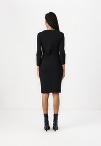 Crna pripijena haljina s tri četvrtine rukava, elegantnog dizajna, zatvaranjem na munju na leđima i rubom do koljena. Nošena s crnim čizmama s petom.