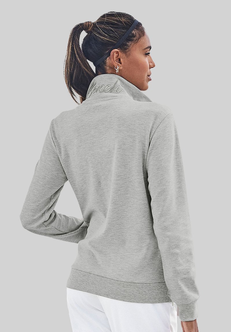 Light grey sweatshirt with a high collar, ribbed cuffs, and hem; features "Bench" embroidered at the back collar. Smooth fabric texture.