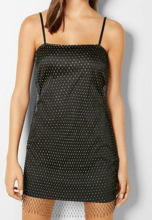 Sort glidende kjole med tynde stropper, satinmateriale, sølvforgyldte diamantmønstrede detaljer og en fiskenet kant.