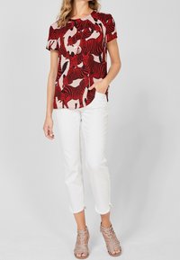 Röd kortärmad topp med svart och krämfärgad zebramönster, kombinerad med vita cropped jeans och metallicklänkar sandaler.