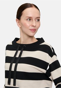 Czarna i kremowa bluzka z paskami, z szerokim dekoltem, z czarnymi sznurkami wykończonymi małymi ćwiekami. Gładka tekstura.