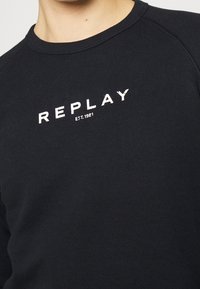 Felpa nera in cotone con scollo rotondo. Presenta la scritta bianca "REPLAY" e "EST. 1981" stampata in un carattere grassetto.