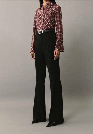 Personne portant une chemise à carreaux bordeaux boutonnée, rentrée dans un pantalon noir taille haute à jambes larges, avec une ceinture noire et des chaussures noires pointues.