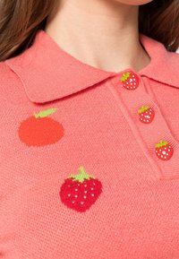 Polo shirt rosa chiaro con disegni di frutta ricamati: un'arancia e molte fragole con dettagli verdi e semi bianchi.