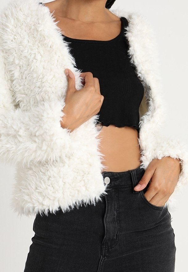 Hvid faux fur cropped jakke med tekstureret, fluffy overflade og åben front, båret over en sort ribbet crop top og højtaljede mørke jeans.