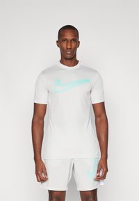 Maglietta sportiva bianca a maniche corte, con un logo Nike azzurro chiaro al centro. Realizzata in materiale liscio e traspirante.