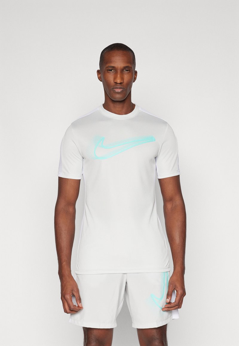 Maglietta sportiva bianca a maniche corte, con un logo Nike azzurro chiaro al centro. Realizzata in materiale liscio e traspirante.