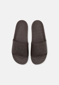 Chanclas marrones con una tira ancha que presenta un logo. La plantilla es texturizada y está moldeada para mayor comodidad, fabricada con material sintético.