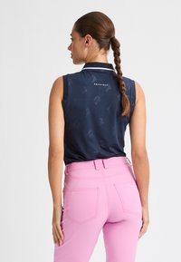 Polo senza maniche blu navy con motivo sottile, caratterizzato da un colletto rialzato e dettagli bianchi, abbinato a pantaloni aderenti rosa con tasche posteriori.