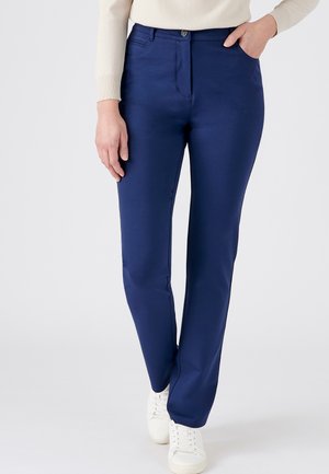 Pantalones azul marino de textura suave, de corte ajustado, con bolsillos frontales y cierre de botón. Combinados con zapatillas blancas.