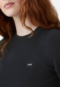 Maglione nero a coste con scollo rotondo e un piccolo logo bianco di Levi's sulla parte sinistra del petto. Texture morbida e design aderente.