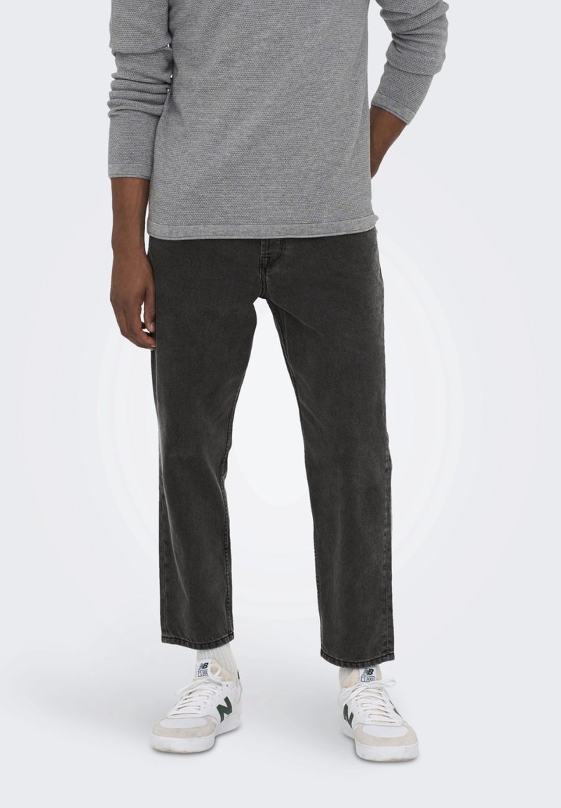 Una camiseta de manga larga gris sobre unos jeans gris oscuro, con un corte relajado. Zapatillas blancas con detalles en verde completan el conjunto.
