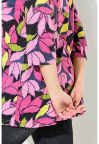 Färgglad tunika med rosa och gröna lövmönster på en svart bakgrund, med avslappnad passform och trekvartslånga ärmar.