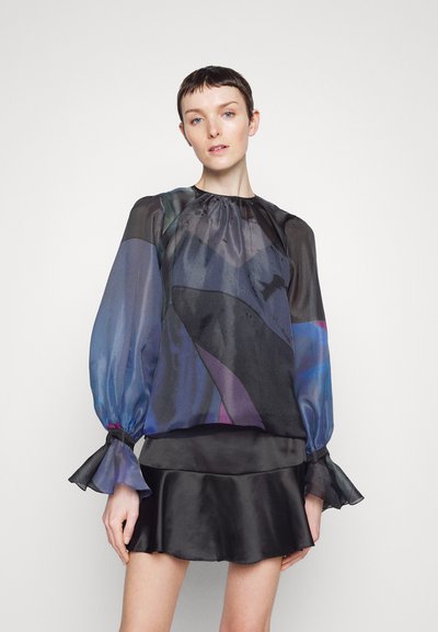 Blouse noire transparente avec un motif abstrait coloré, manches bouffantes, poignets élastiques et un ourlet volanté sur une jupe noire ajustée.
