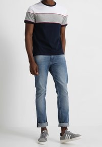 Camiseta de manga corta con bloques de color en azul marino, gris y blanco; combinada con jeans azul claro con los puños enrollados y zapatillas grises con rayas blancas.