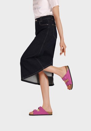 Sandali rosa in suede con cinturini a doppia fibbia, indossati con una gonna maxi in denim nera caratterizzata da un orlo grezzo e cuciture a contrasto.