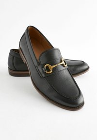 Černé kožené loafers s texturovaným povrchem, s akcentem zlatavé spony a kulatou špičkou. Hnědé detaily na podrážce.