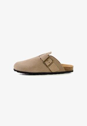 Beiger Wildleder-Slipper mit verstellbarer seitlicher Schnalle, Kork-Fußbett und schwarzer strukturierter Sohle, gezeigt auf weißem Hintergrund.