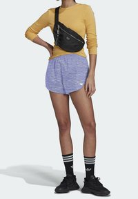 Keltainen pitkähiha, musta olkalaukku, violettihousut joissa valkoinen aalto-kuvio, mustat lenkkarit ja mustat raidalliset sukat.