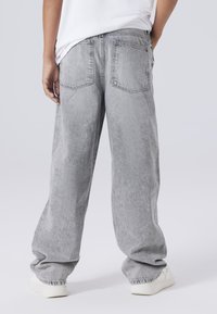 Sive traperice imaju opušteni, široki kroj, stražnje džepove i izblijedjeli izgled, uparen s bijelim tenisicama.