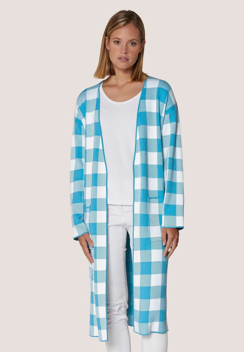 Lange cardigan in blauw-witte ruitpatroon, brei stof, open voorkant ontwerp, en lange mouwen. Draag dit over een witte top en broek.