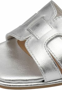 Sandale métallique argentée avec un design à large bride, texture lisse, semelle plate et fermeture Velcro pour un ajustement facile.