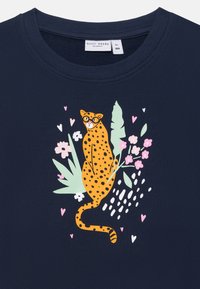 Sweatshirt blu navy con una grafica di una leopardessa arancione con occhiali, circondata da foglie verdi e fiori rosa, con una finitura texturizzata.