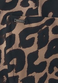 Leopardin kuosi kangas vaaleanruskeassa ja mustassa värissä, jossa on sileä rakenne ja pieni metallinen logo-akkentti.