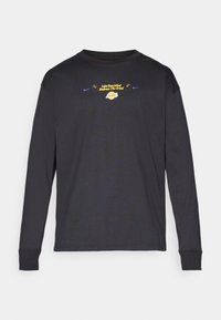 Juodas ilgomis rankovėmis marškinėliai, pagaminti iš medvilnės. Priekyje yra geltonas ir purpurinis tekstas su Lakers logotipu. Apvalus kaklas ir rankovės su užlenkimu.