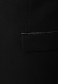Musta kangas, millel on sile tekstuur, ning millel on ristkülikukujuline tasku, millel on peen hall äär. Minimalistlik disain, ilma nähtava riistvara või mustriteta.