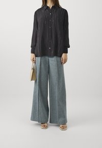 Černá dlouhá košile s vertikálními bílými pruhy, kombinovaná s širokými světle modrými džíny. Outfit doplňuje malá béžová taška.