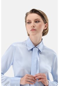 Light blue satin shirt with a pointed collar, long sleeves, and a tie detail at the neck. Smooth texture with a glossy finish.