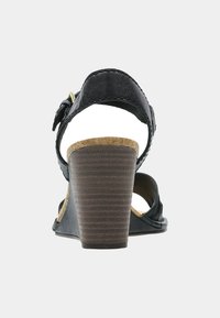 Sandale compensée en cuir noir avec une semelle en liège texturé et un talon marron cranté. Elle possède une sangle ajustable à la cheville avec une boucle dorée.