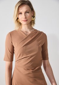 Brun tilpasset kjole med korte ermer, som har et omslag design og glatt tekstur. Store gulløredobber gir en kontrasterende aksent.