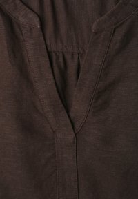 Tissu en lin brun foncé avec un col en V et des détails de couture subtils autour du col.