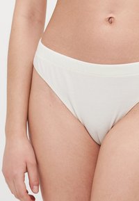 Bijela rebrasta bikini gaćice s mekim, širokim pojasom i minimalnim pokrićem. Tkanina je glatka s suptilnom teksturom.