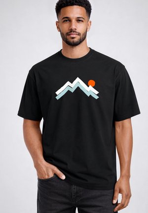 Man wearing black T-shirt with a stylized mountain graphic in white and light blue, with an orange sun near the peak.