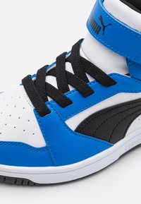 Basket montante Puma en cuir blanc, bleu et noir, lacets noirs, bout perforé et logo Puma sur la bride de cheville.