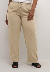Pantalons large beige avec une taille élastique et un cordon de serrage, dotés de poches latérales et d'un tissu doux et texturé.