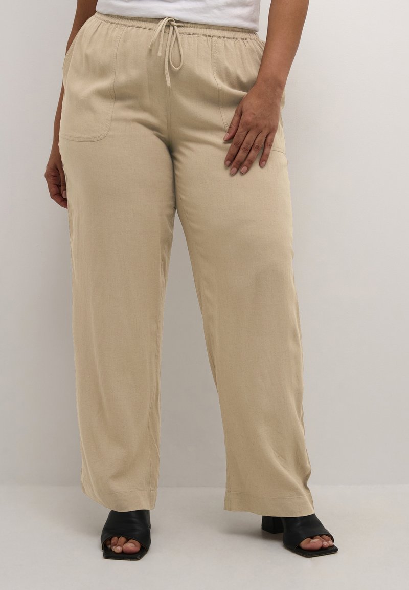 Pantalons large beige avec une taille élastique et un cordon de serrage, dotés de poches latérales et d'un tissu doux et texturé.