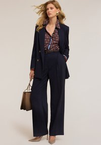 Námořnický oblek na míru s kalhotami širokého střihu a vzorovanou blůzou. Obsahuje výrazný límec, hnědý kožený pásek a hnědou kabelku.