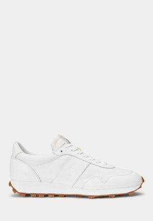 Λευκό χαμηλό αθλητικό παπούτσι με λευκά κορδόνια, υφασμένο δερμάτινο επάνω μέρος και καφέ ραβδωτή σόλα, εμφανίζεται στο προφίλ πλευράς σε απλό φόντο.