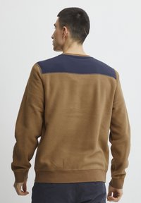 Sudadera de polar marrón con un panel de hombro en azul marino, ribetes en el dobladillo y puños acanalados. Textura suave, corte casual y diseño minimalista.
