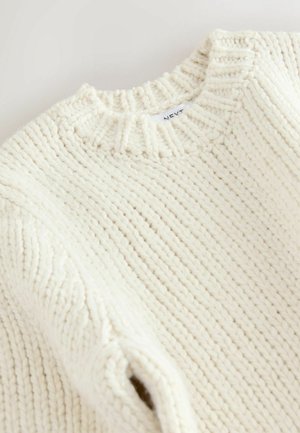 Kremno barvana pletena majica z ribanim okroglim ovratnikom in teksturiranim vzorcem. Preja izgleda debela in mehka.