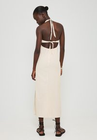 Knie-langes, ärmelloses Kleid in Creme mit dünnen, vertikalen Streifen, offener Rückseite und Halfter-Nackenschnürung. Mit seitlichem Schlitz und glatter Textur.
