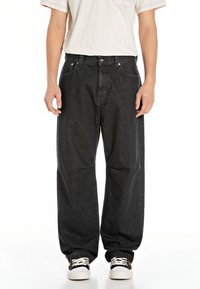Svarte denimbukser med løs passform, som har fem lommer og knappelukking. Brukes med svart og hvite sneakers.